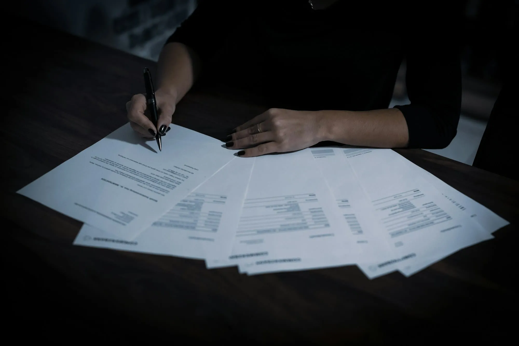 Persona firmando varios formularios administrativos sobre una mesa